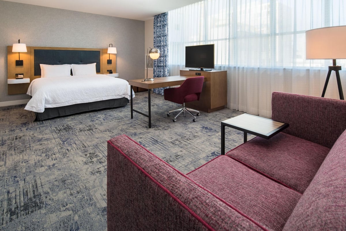 A hotel room with a bed, desk, TV, and seating area.