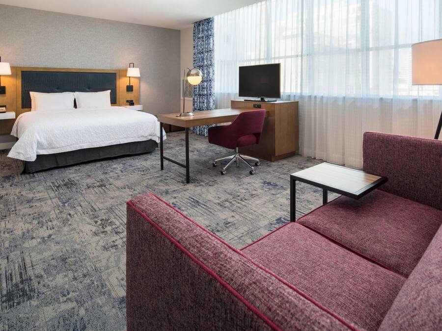 Quarto de hotel com cama, escrivaninha, televisão e área de estar.