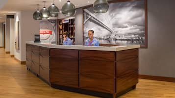 A hotel reception desk with a large framed picture of a bridge, wooden paneling, and pendant lighting.