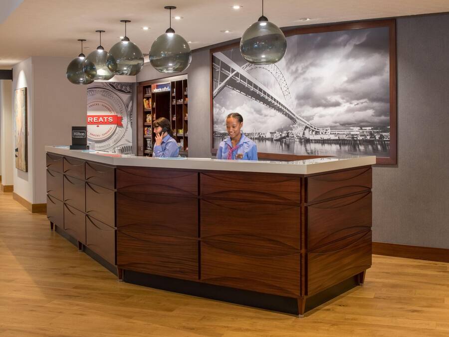 A hotel reception desk with a large framed picture of a bridge, wooden paneling, and pendant lighting.