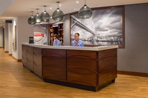 Un comptoir d’accueil d’hôtel orné d’un grand tableau encadr é représentant un pont, avec un lambris en bois et des luminaires suspendus.