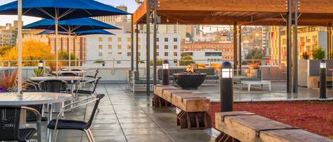 An outdoor patio with tables and chairs, a fire pit, and umbrellas.