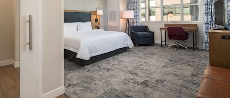 Habitación de hotel con cama, escritorio, silla y ventanas amplias.