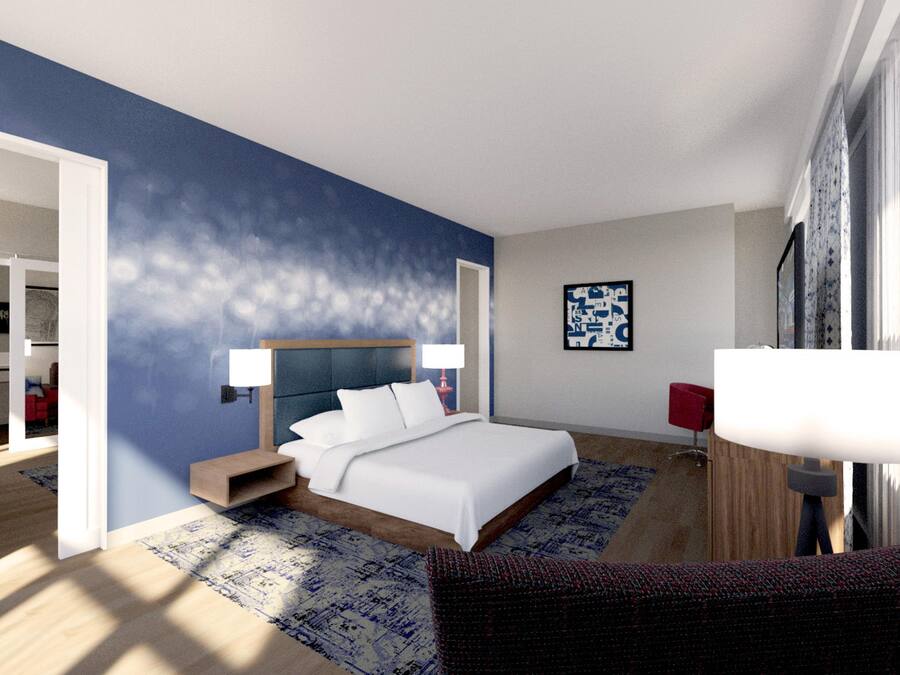 Habitación de hotel moderna con una cama grande, lámparas de noche, una silla roja y vistas al baño contiguo.