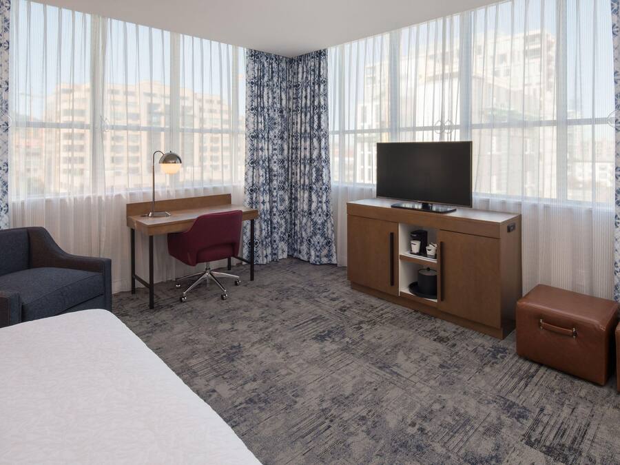 A hotel room with a bed, a desk with a chair, a television, a wardrobe, and two suitcases.