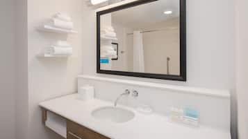 Un baño moderno con un lavamanos blanco, un espejo y repisas con toallas dobladas.