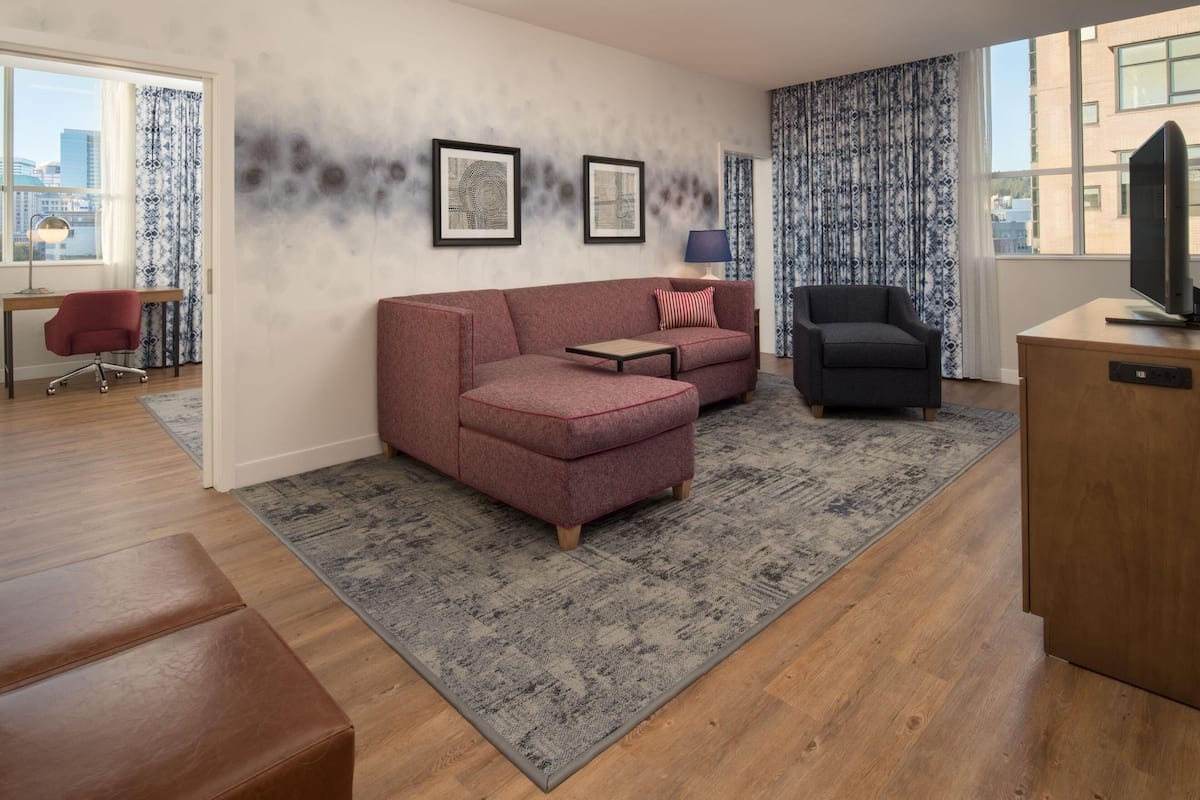 A modern living room with a sofa, armchair, TV, and city view.