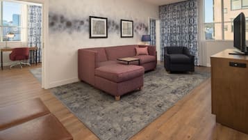 Una sala de estar moderna con sofá, sillón, televisor y vista a la ciudad.