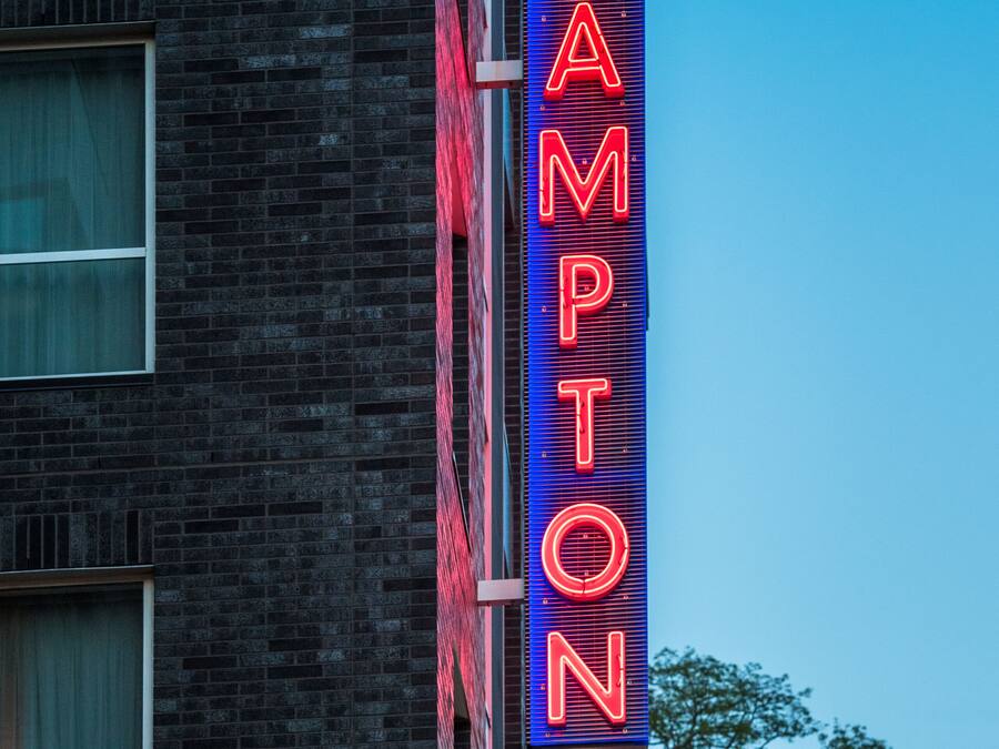 En neonskylt på en byggnad med texten ”HAMPTON by Hilton”.