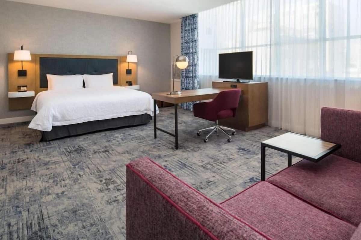 A hotel room with a bed, desk, chair, and TV.