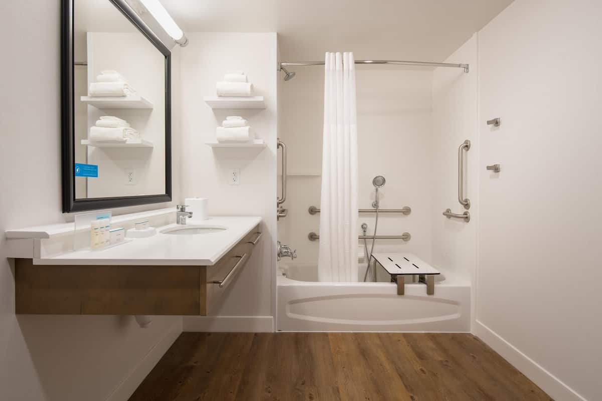 A modern bathroom with a double sink vanity, a large mirror, a bathtub, and a shower with a curtain.