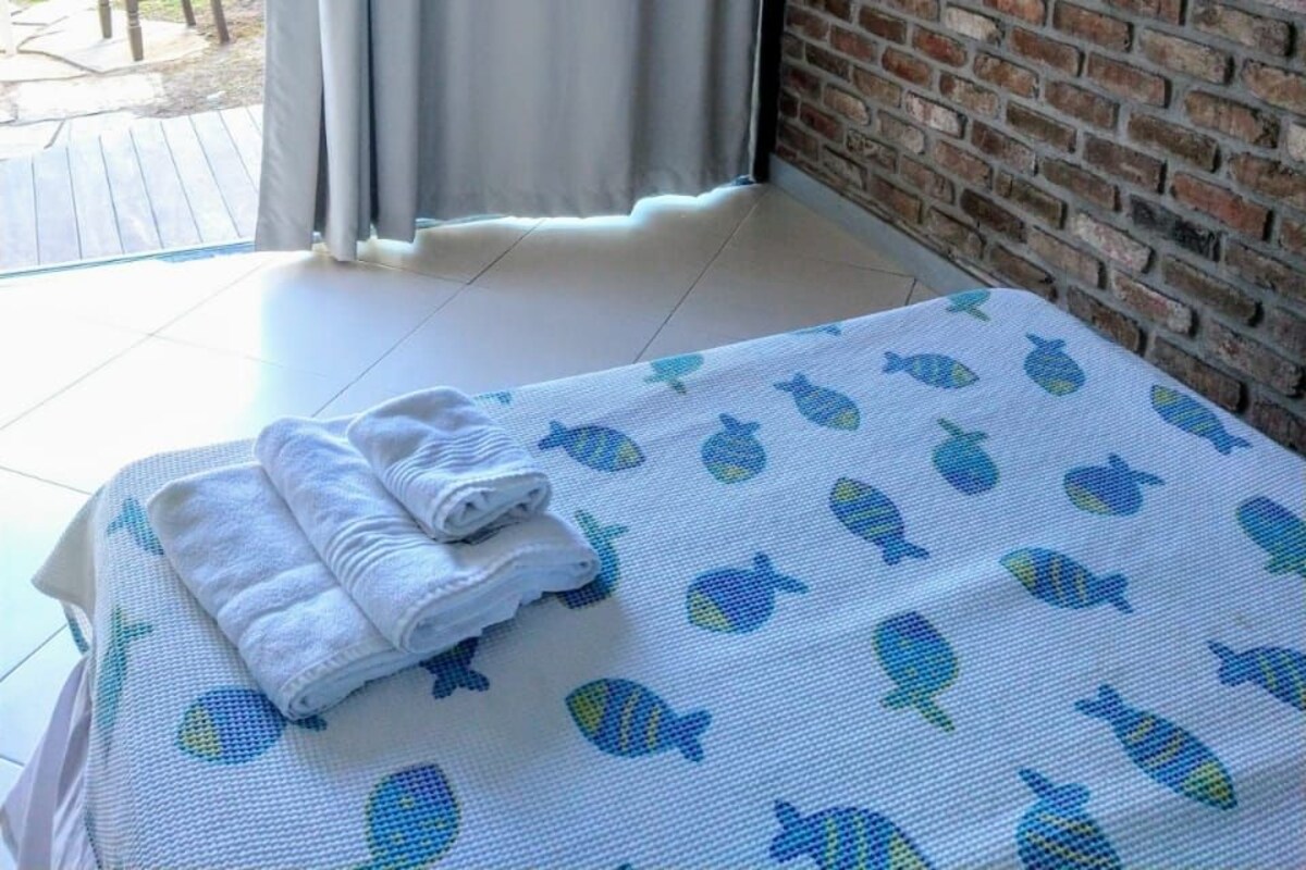A bedroom with a bed, a TV mounted on a brick wall, and a view of the outdoors.