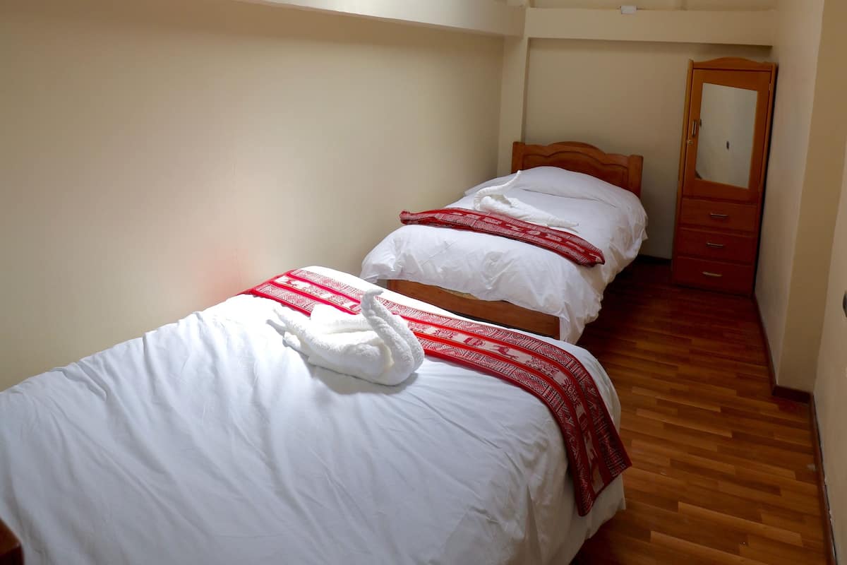 A narrow room with two beds, wooden beams on the ceiling, and a wooden wardrobe.