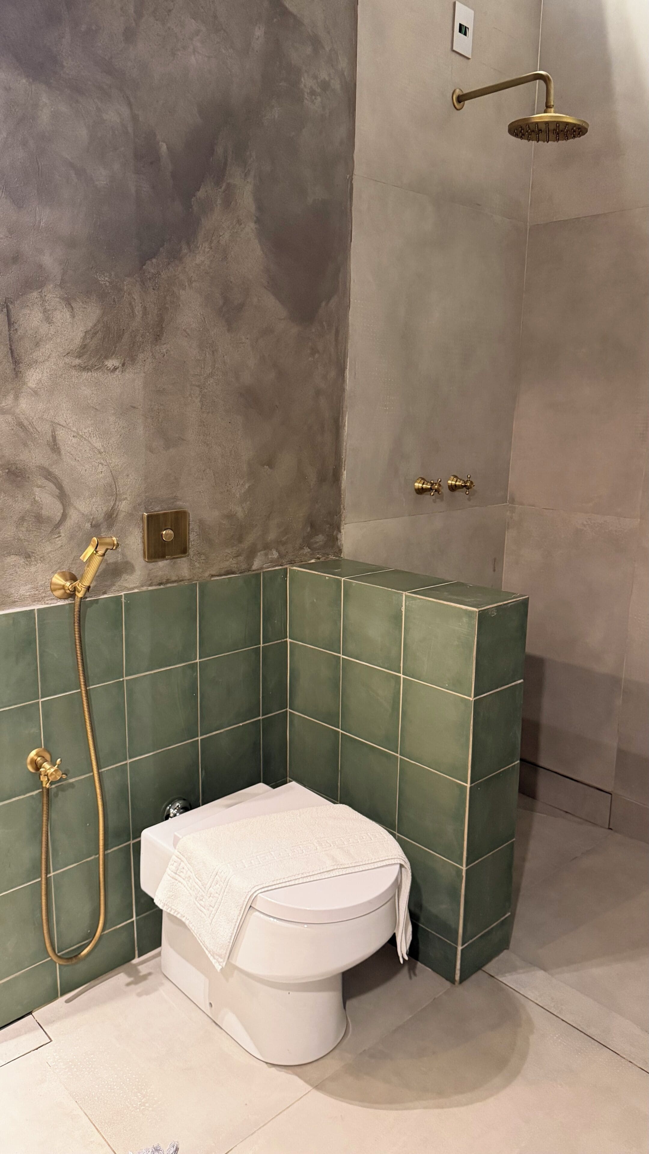 A bathroom with a toilet, green tiles, a shower, and a textured wall.
