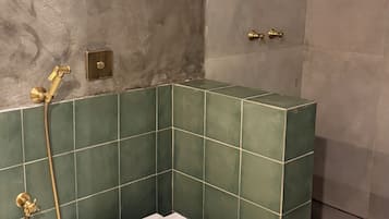 Un baño con inodoro, azulejos verdes, ducha y pared con textura.