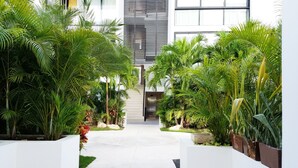 A modern building with a central staircase, surrounded by lush greenery and white walls. - Anah Suites - Las Flores Properties (Playa del Carmen)