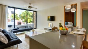 A modern living room with a sofa, a coffee table, and a kitchen area with a fruit bowl. - Anah Suites - Las Flores Properties (Playa del Carmen)