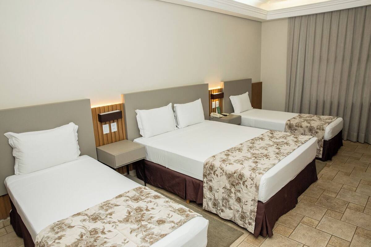 Ein Hotelzimmer mit vier Einzelbetten, jeweils mit Kopfteil, Nachttischen und Lampen.