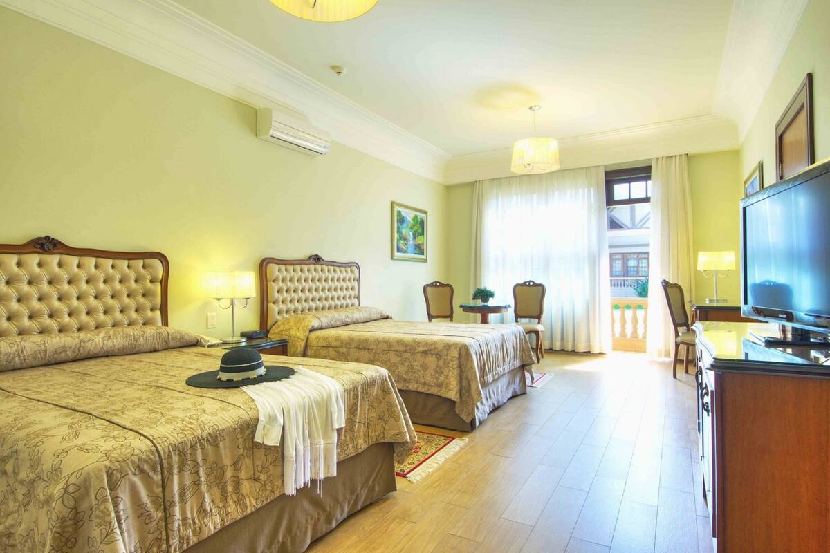 Ein Hotelzimmer mit zwei Betten, einem Fernseher, einem Schreibtisch und einem Balkon mit Vorhängen.