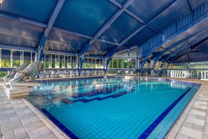 Una piscina con plataforma de azulejos, una estatua y una zona cubierta con asientos.