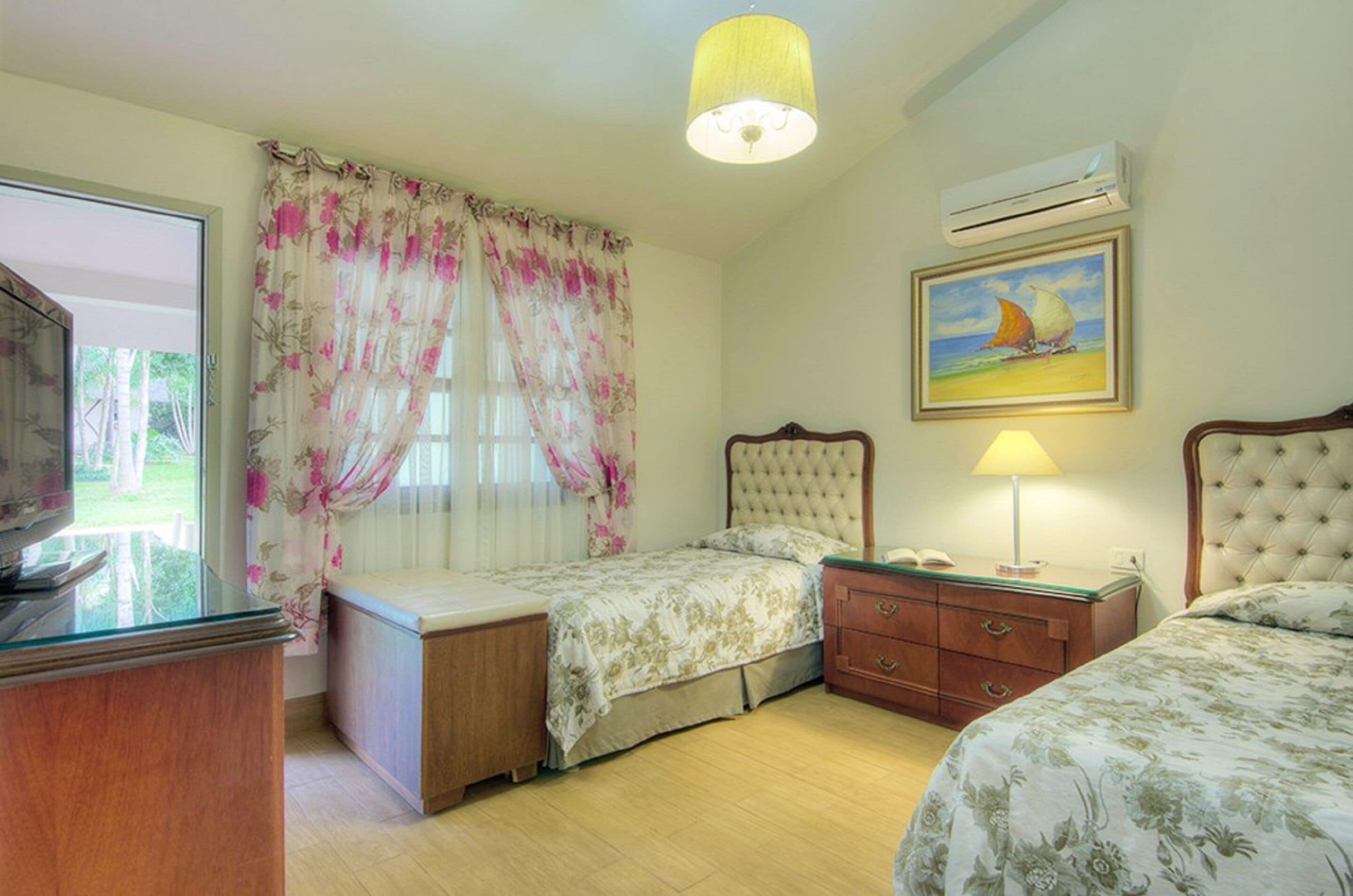 Una camera da letto con due letti, un comodino, una lampada, una TV e un quadro appeso al muro.