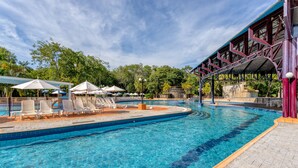 A swimming pool with lounge chairs and umbrellas, surrounded by trees and a covered area with a metal roof.