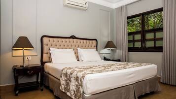 A neatly arranged bedroom with a large bed, two bedside tables, a window with curtains, and an air conditioning unit on the wall.