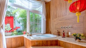 A bathroom with a large window, wooden walls, a bathtub, and a vanity with a vase of flowers.