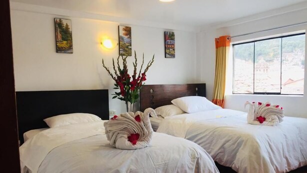 A hotel room with two beds, a large window, and artwork on the walls. - Qori punku - Hostel (Cusco)