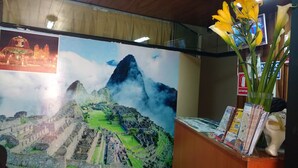 A reception desk with a large poster of Machu Picchu, a vase with yellow flowers, and various brochures. - Qori punku - Hostel (Cusco)