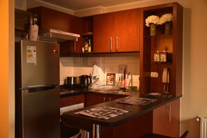 A compact kitchen with wooden cabinets, a stainless steel refrigerator, a coffee maker, and a small sink.