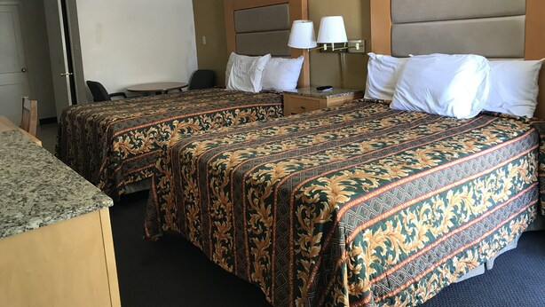 A hotel room with two beds, a desk, a chair, and a small table.