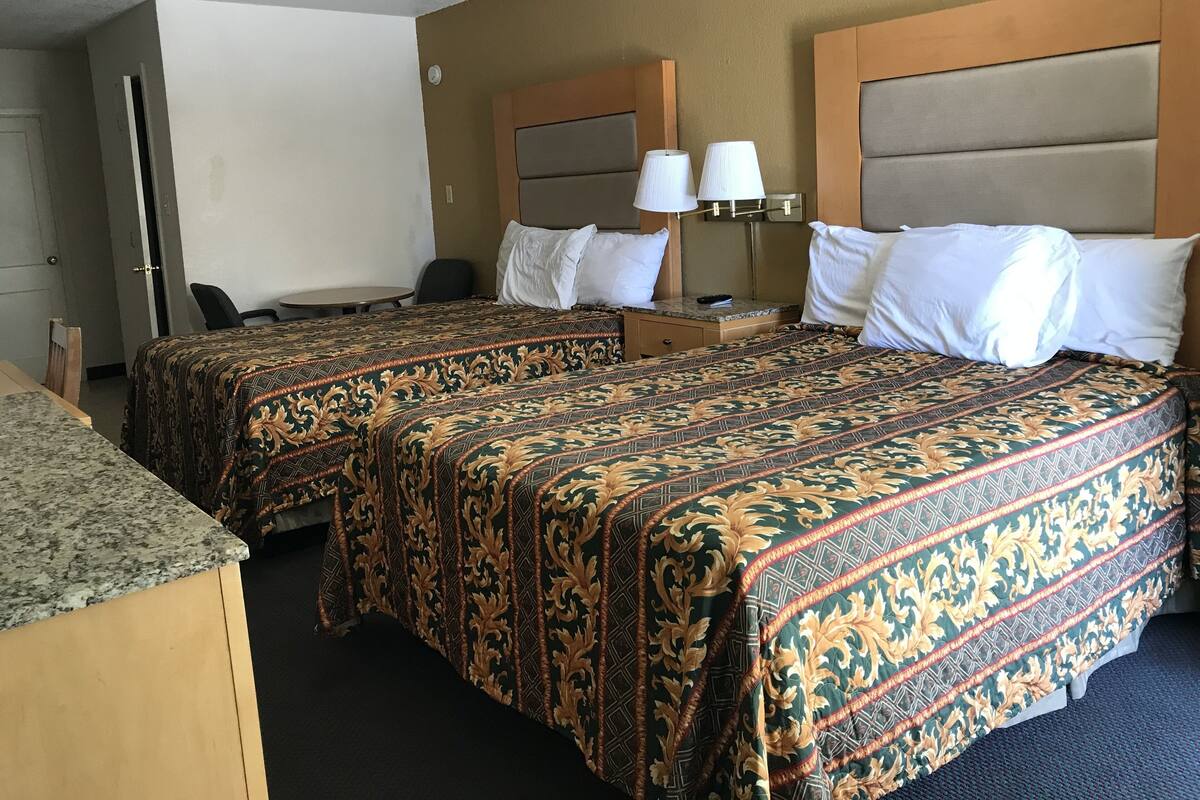 A hotel room with two beds, a desk, a chair, and a small table.