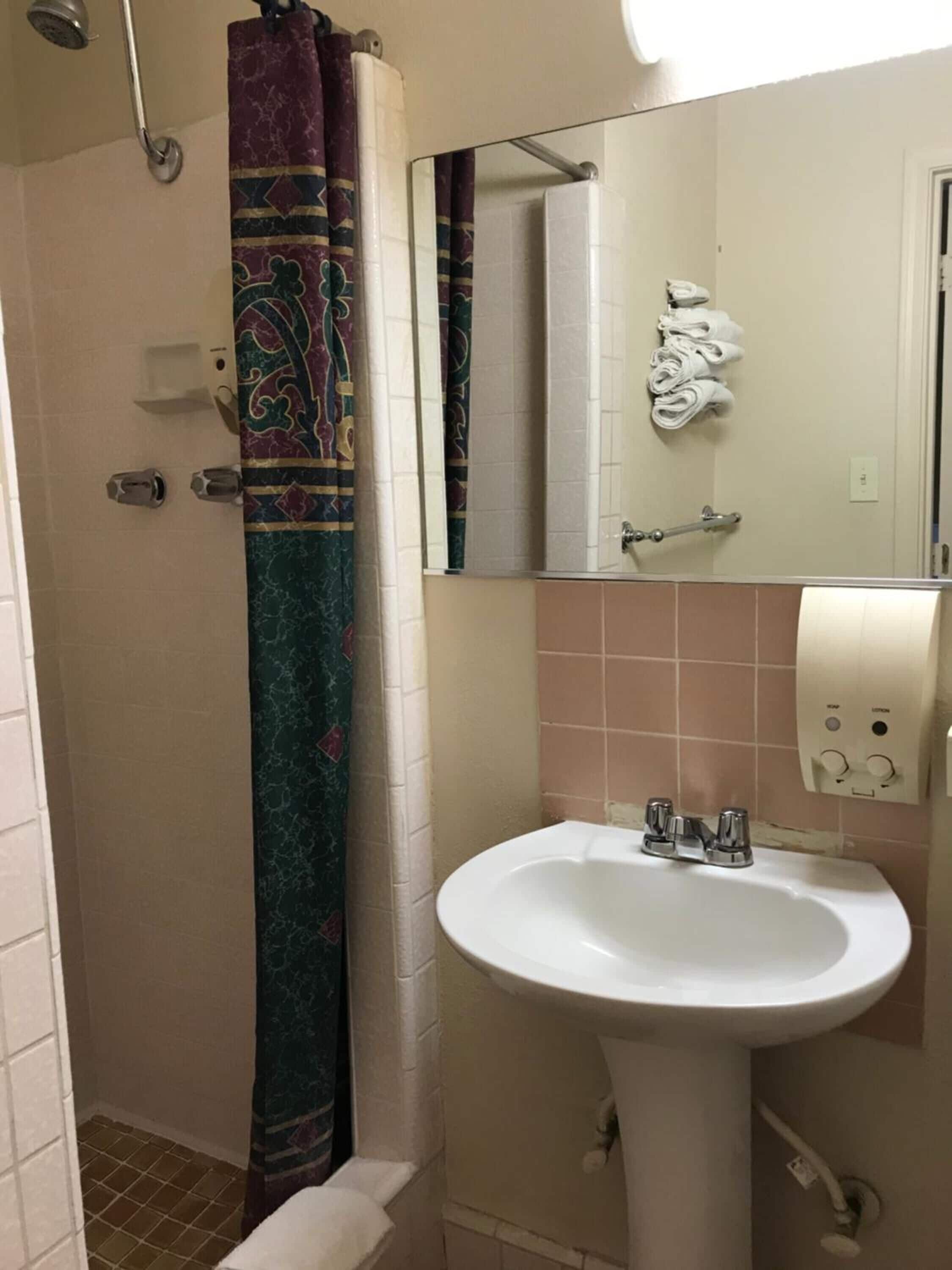 A bathroom with a shower, a sink, a mirror, and a towel rack.