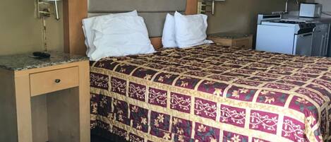 Habitación de hotel con cama, dos mesitas de noche, escritorio, kitchenette pequeña y luz de techo.
