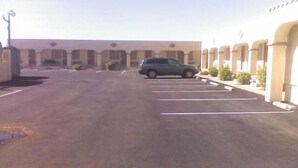 A parking lot with a single SUV parked in the middle. There are multiple parking spaces, and the lot is adjacent to a building with a beige facade and a series of columns.