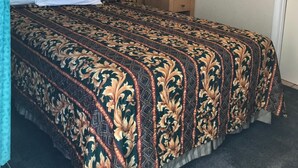 A hotel room with a bed, a nightstand, a lamp, and a door.