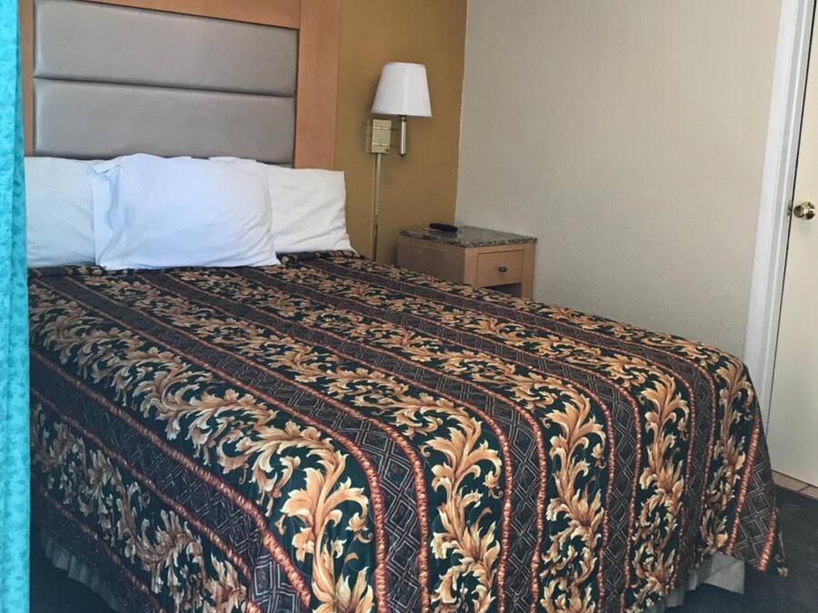 A hotel room with a bed, a nightstand, a lamp, and a door.