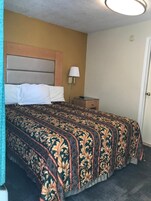 A hotel room with a bed, a nightstand, a lamp, and a door.