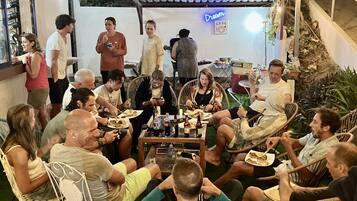 A group of people seated around a table in an outdoor setting, possibly a restaurant or cafe, with a sign reading "Dream Cafe" in the background.