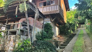 Una casa de madera rústica con balcón, pared de piedra y una palmera.