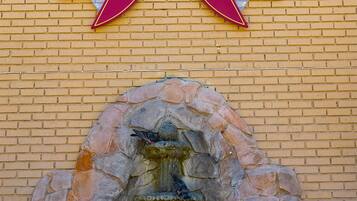 A stone fountain with a decorative arch, a sun emblem, and a pair of red ribbons on a brick wall.