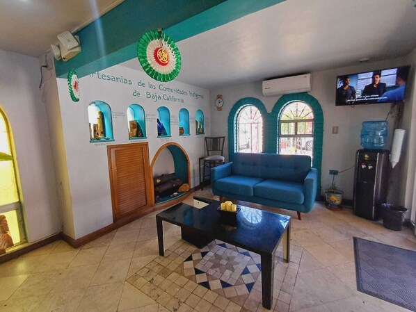 Una sala de estar con un sofá azul, una mesa de centro y una pared que exhibe comunidades indígenas de Baja California.