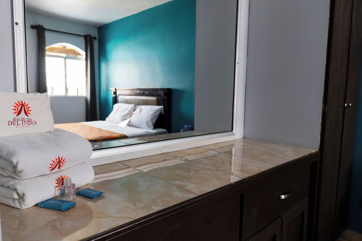 A hotel room with a bed, a window, and a bathroom counter with towels and toiletries.