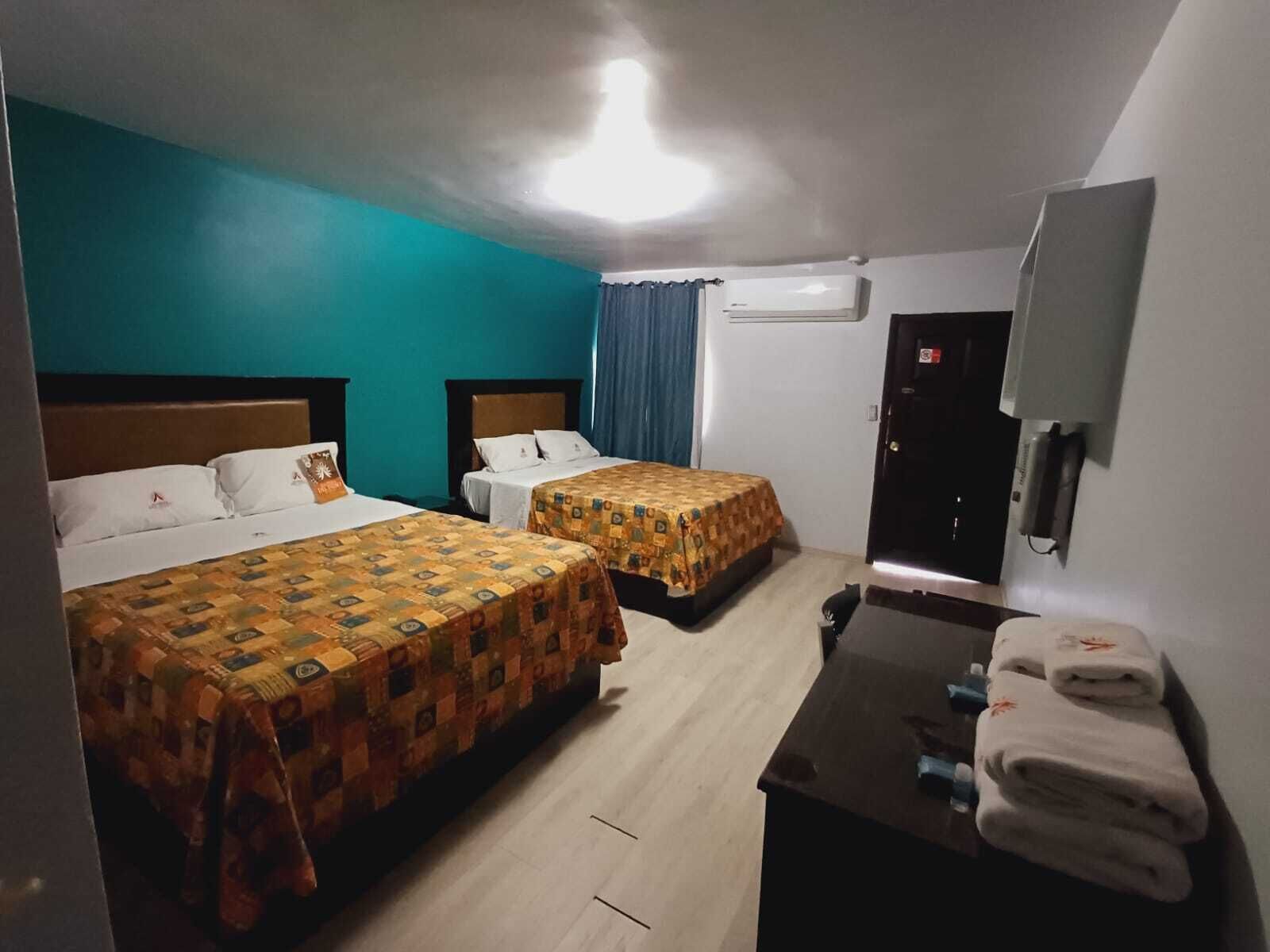 Habitación de hotel con dos camas, un escritorio con silla, televisión y aire acondicionado.