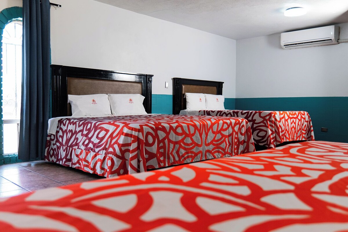 A hotel room with two beds, a window with curtains, and an air conditioning unit on the wall.