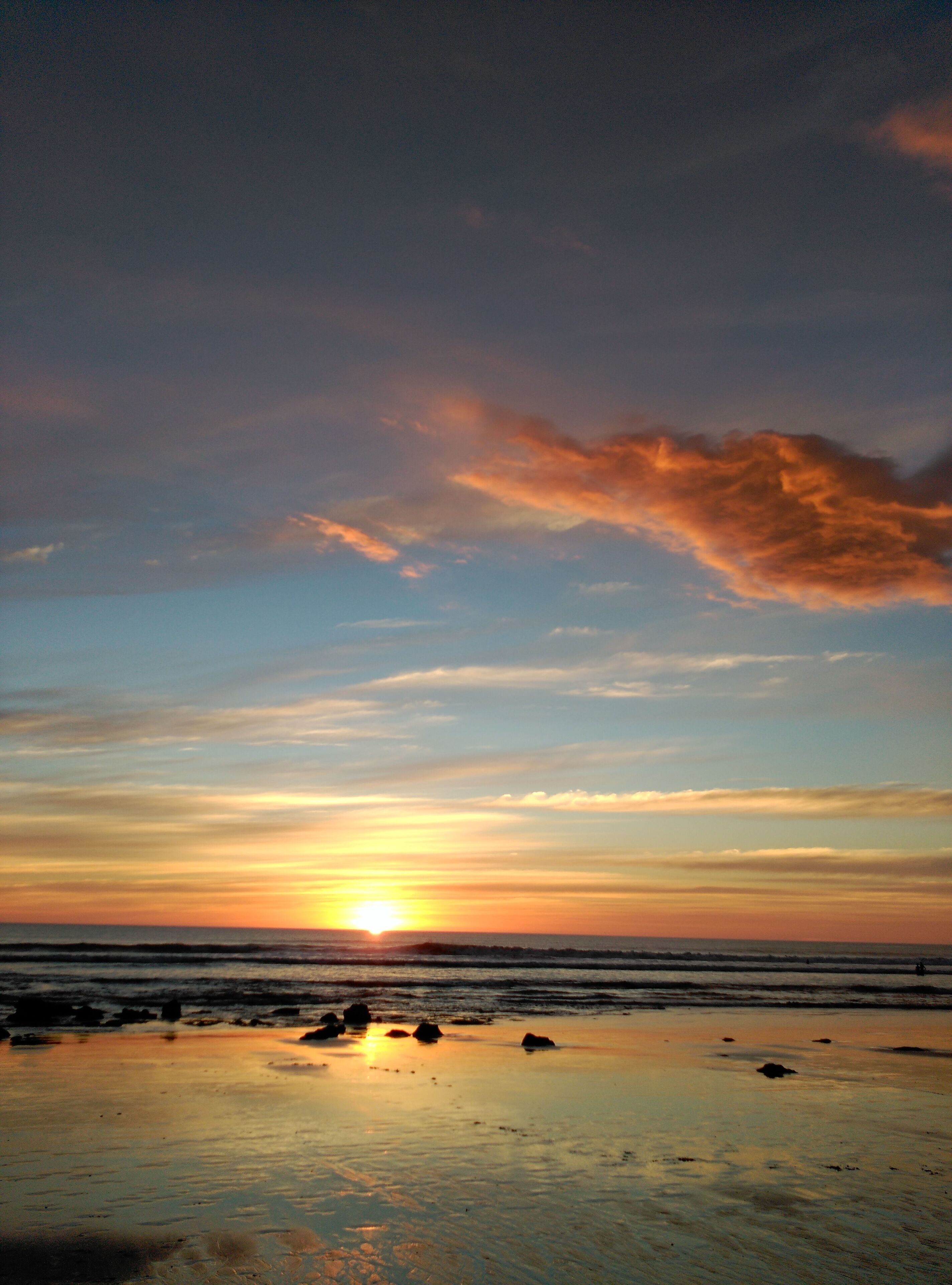 Ein Strand bei Sonnenuntergang, die Sonne tief am Horizont, sanfte Wellen am Ufer und ein klarer Himmel.