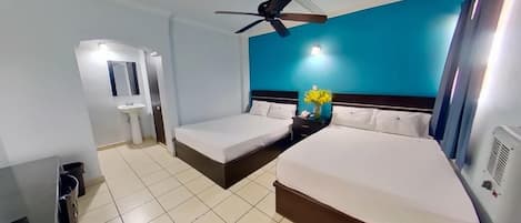 A hotel room with a bed, a bedside table, a nightstand, a ceiling fan, a wall-mounted TV, and a bathroom with a sink and mirror.