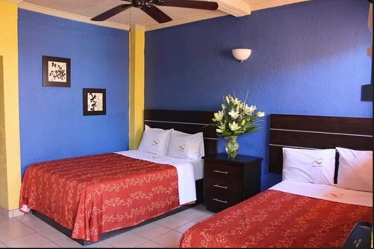 Habitación de hotel con dos camas, una mesita de noche con un jarrón de flores y cuadros en la pared.