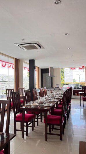 A dining area with a long table set for a meal, surrounded by wooden chairs with red cushions.